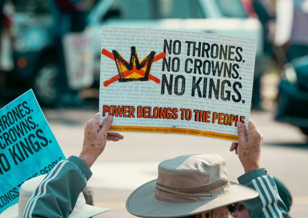 This image highlights a No Kings protestors sign. The sign is their voice for the world to see what they are advocating for while they march along others.