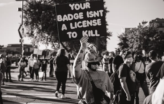 This photo shows a protest against police brutality, with a person holding a sign reading, "Your badge isn't a license to kill." This reflects the sentiment of those protesting against ICE's recent actions.